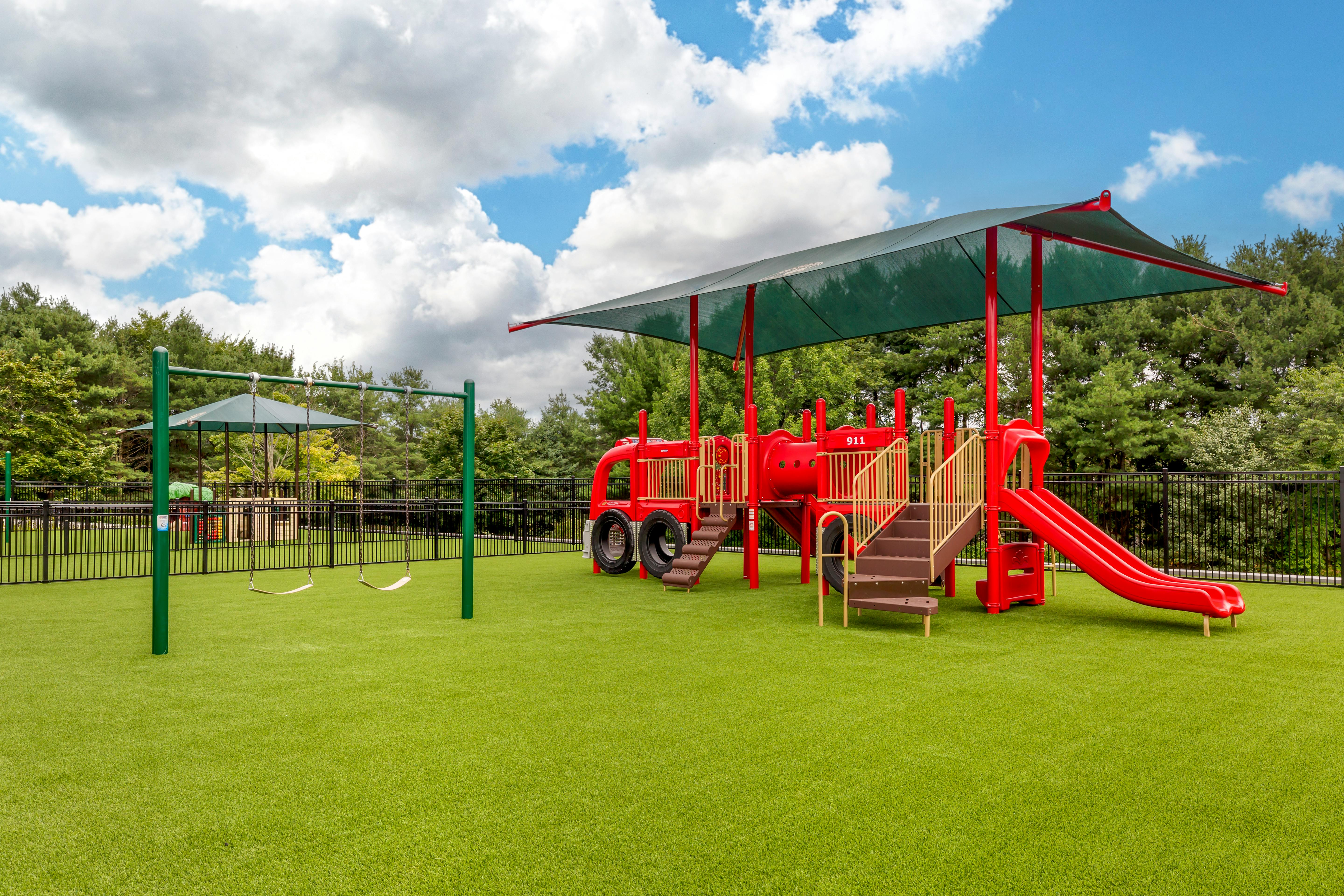 A red playground structure with a slide, steps, and swings on green turf