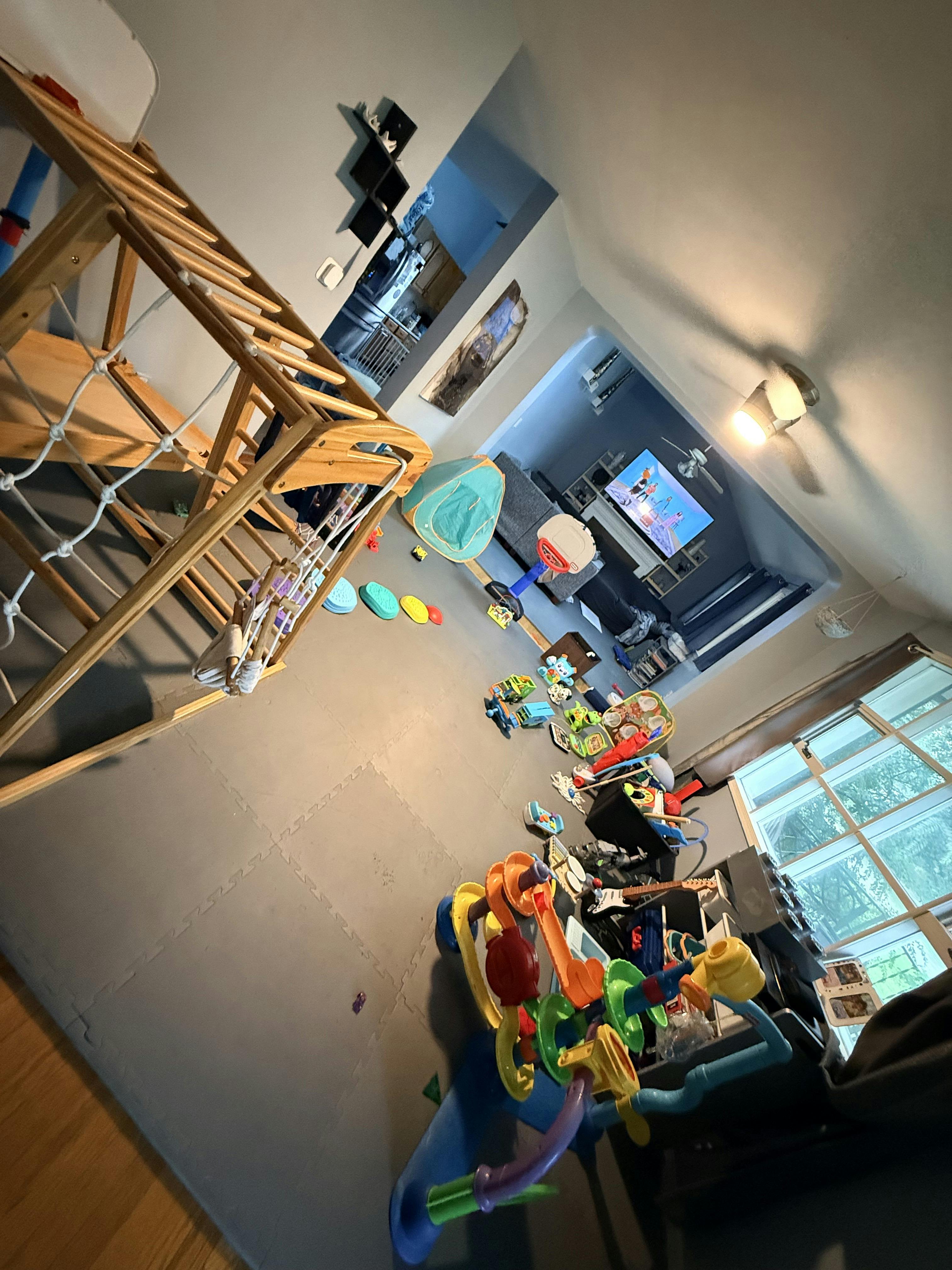 Playroom with a wooden climbing frame and various toys on a foam floor