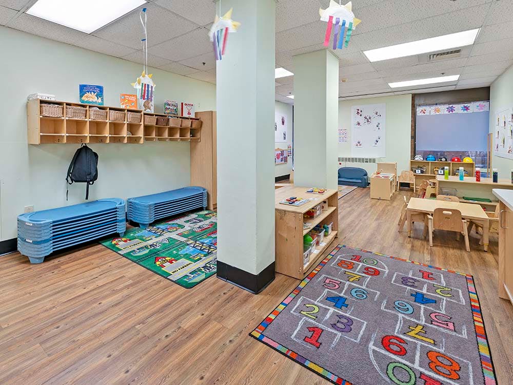 Childcare room with cubbies, small tables, and play rugs