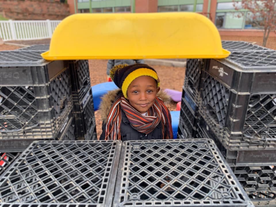 Child peeking from behind stacked crates with a yellow cover