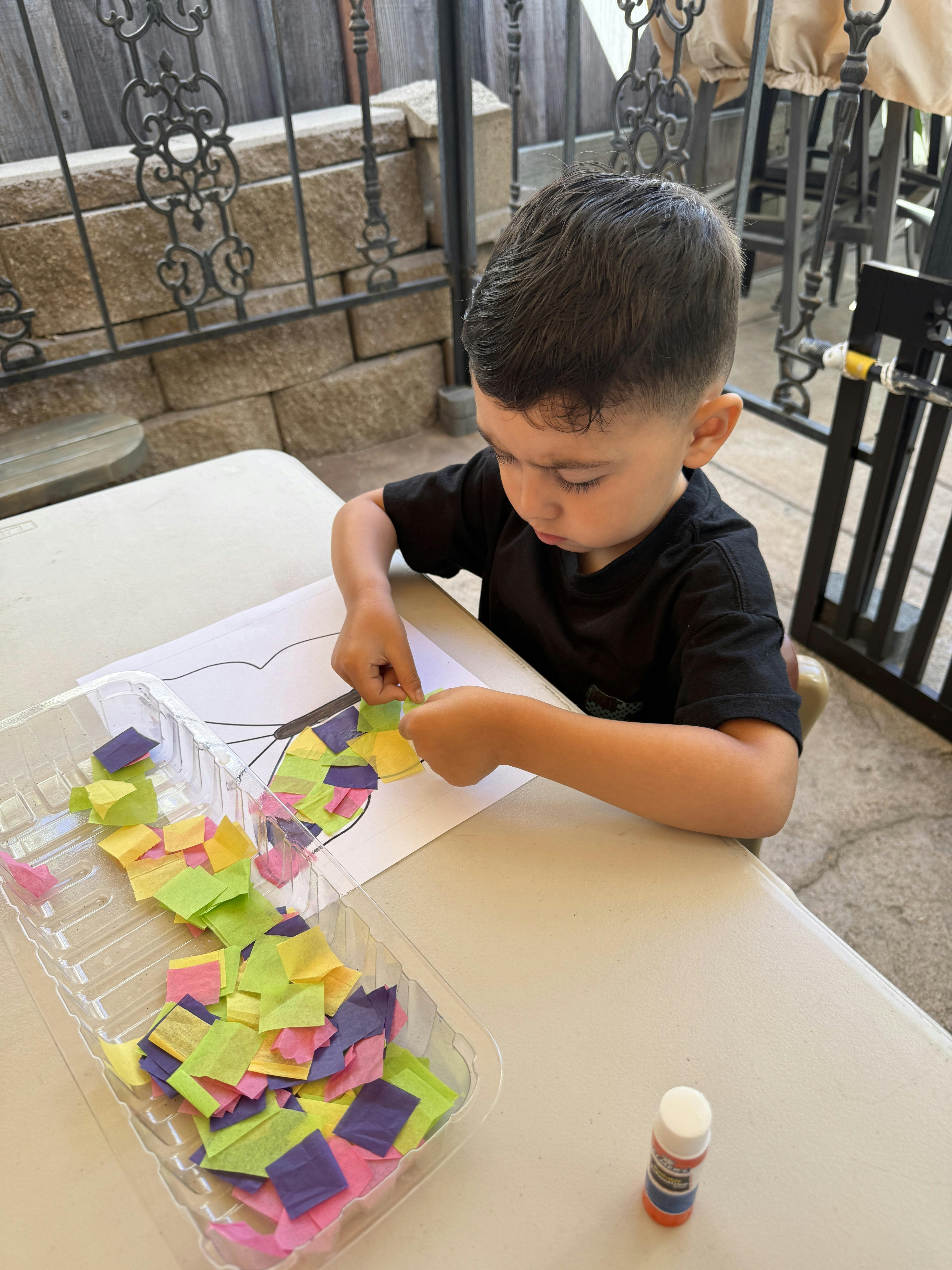 Child doing a craft with colorful paper pieces and glue stick