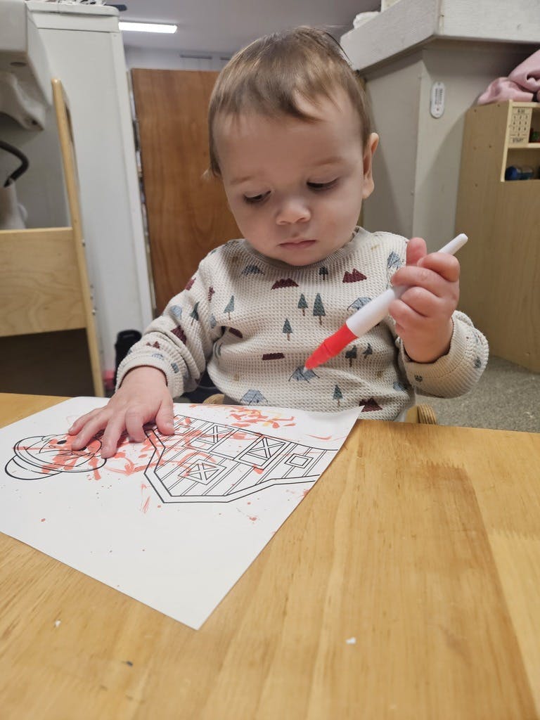 Child coloring on paper with a red marker