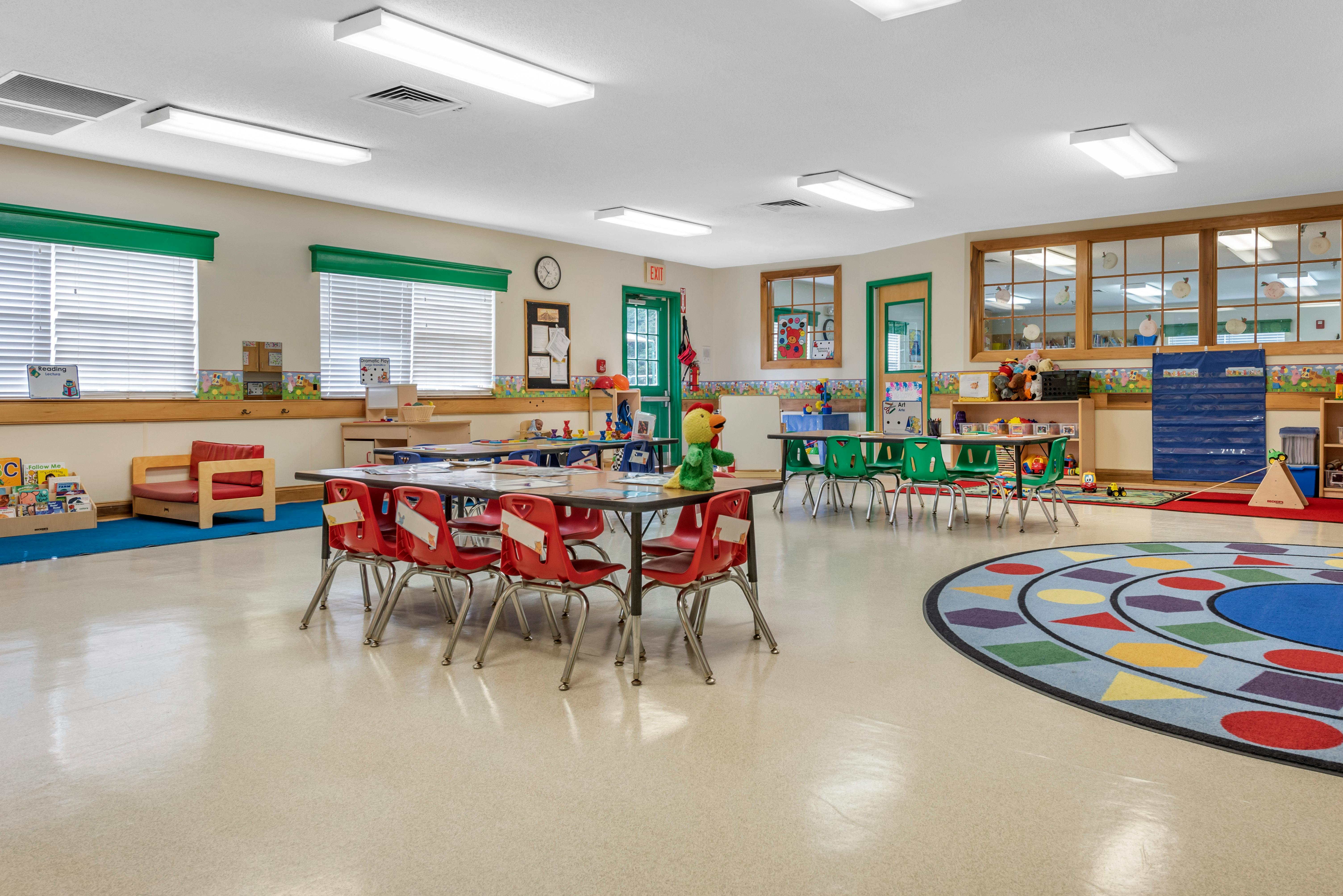 Classroom with child-sized tables and chairs, a reading corner, and a colorful rug