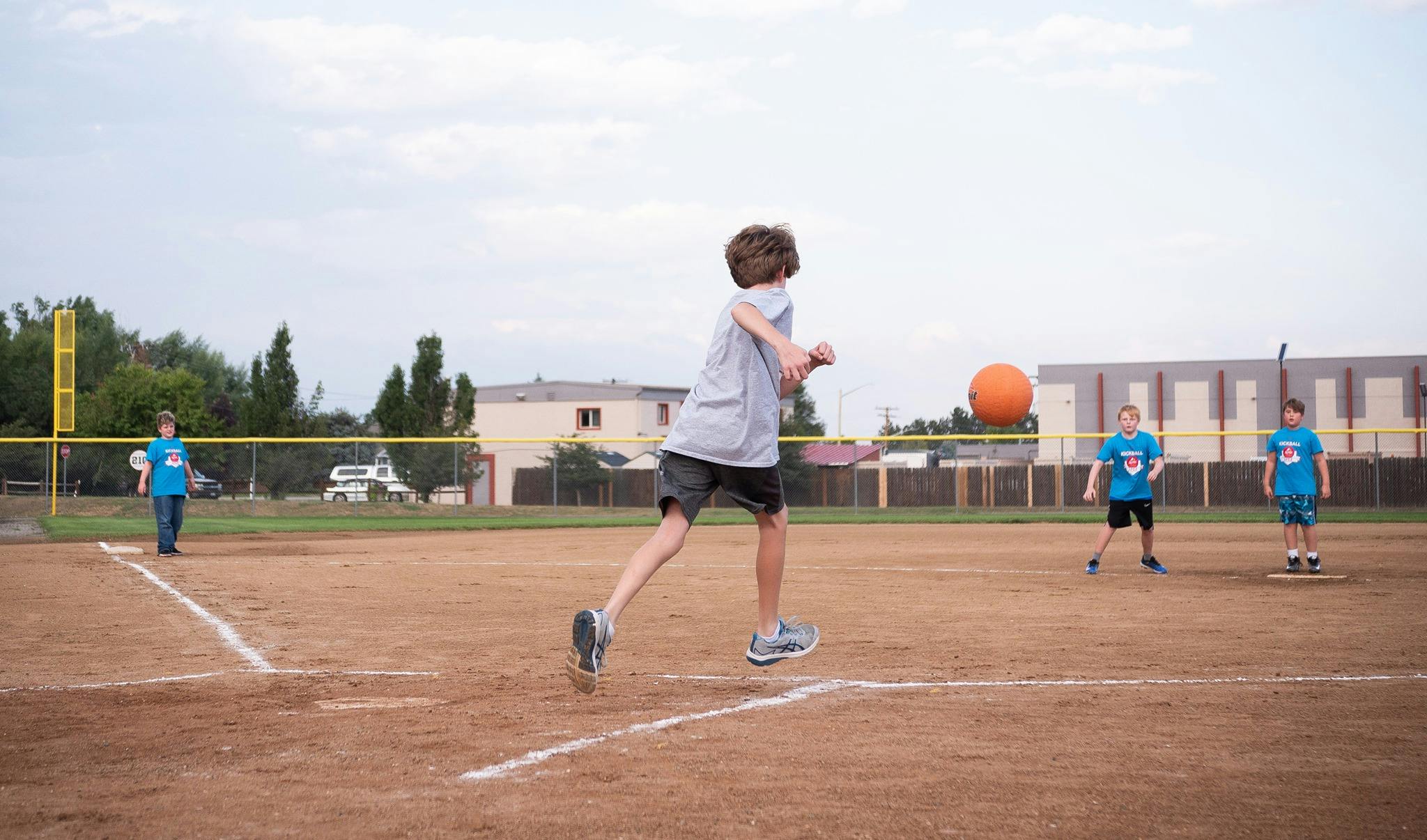 Child kicking an orange ball on a baseball field with other children