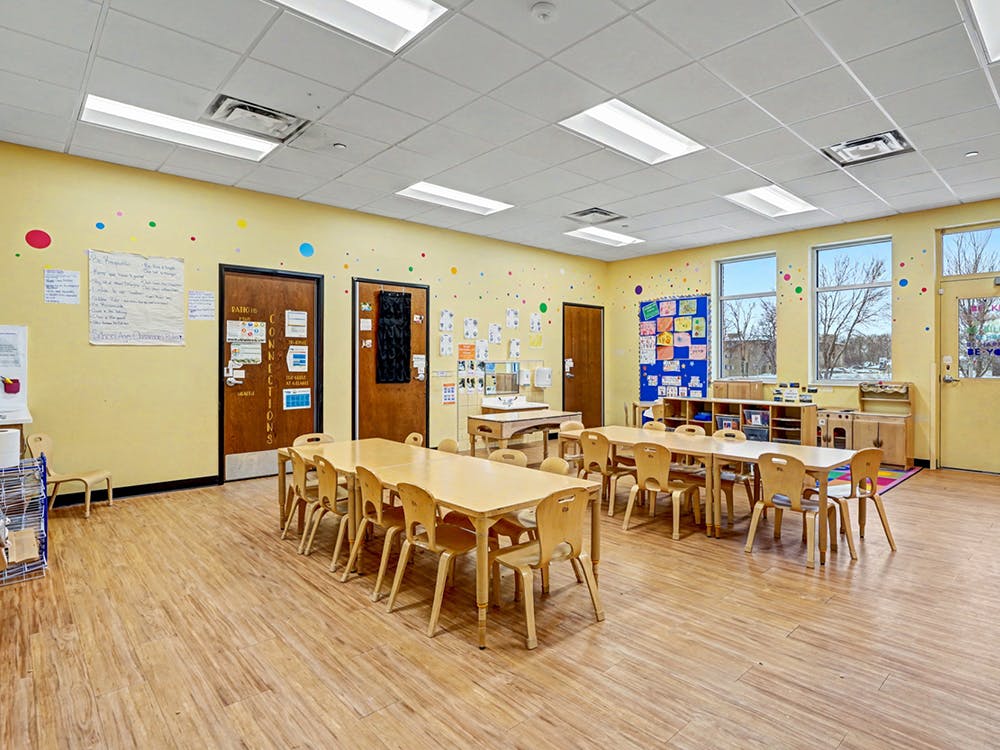 Empty classroom with yellow walls, small tables, and chairs