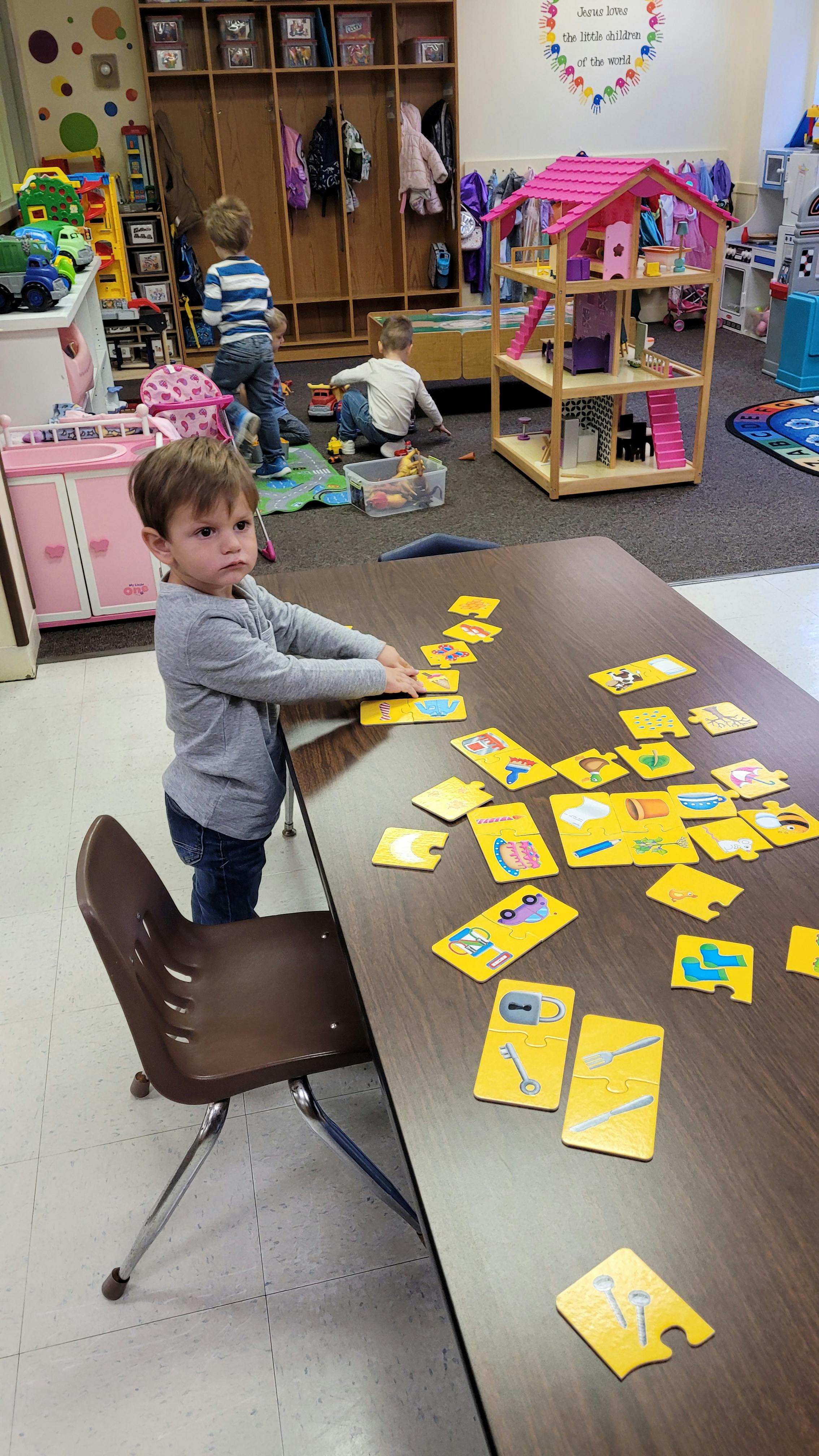 Child standing at a table playing with yellow puzzle pieces in a classroom