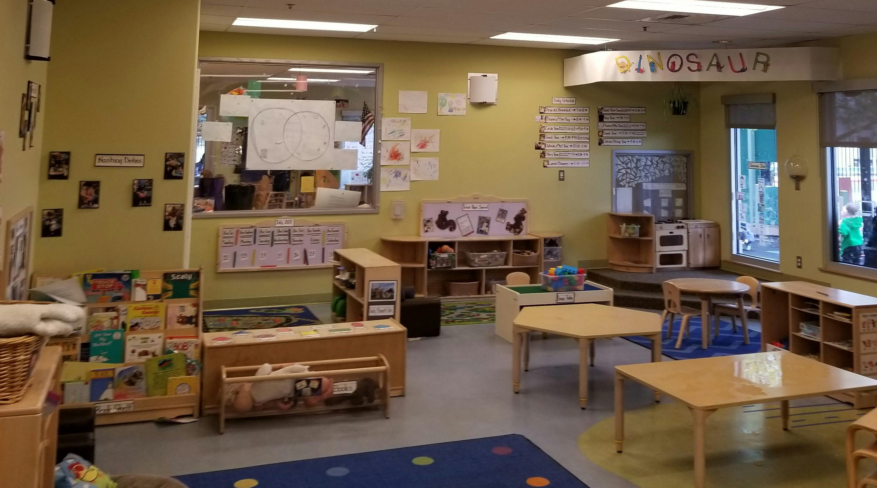 Children's classroom with small tables, chairs, bookshelves, and a play kitchen