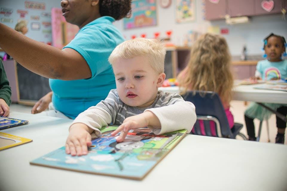 Child playing with a puzzle at a table in a classroom