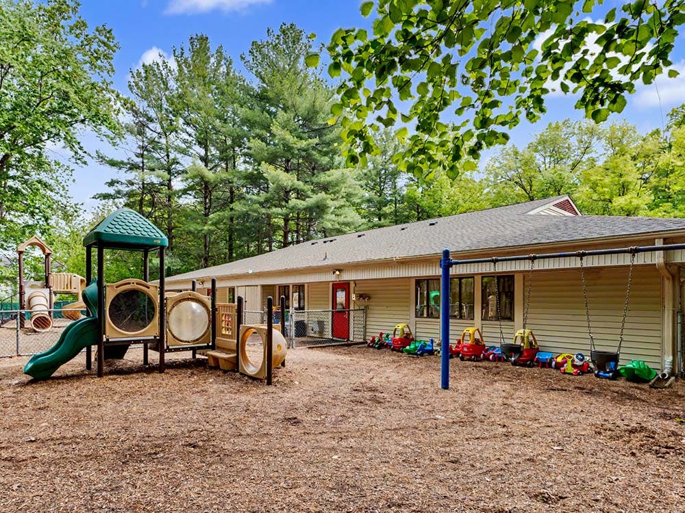 Playground with swings, slides, and ride-on toys next to a building