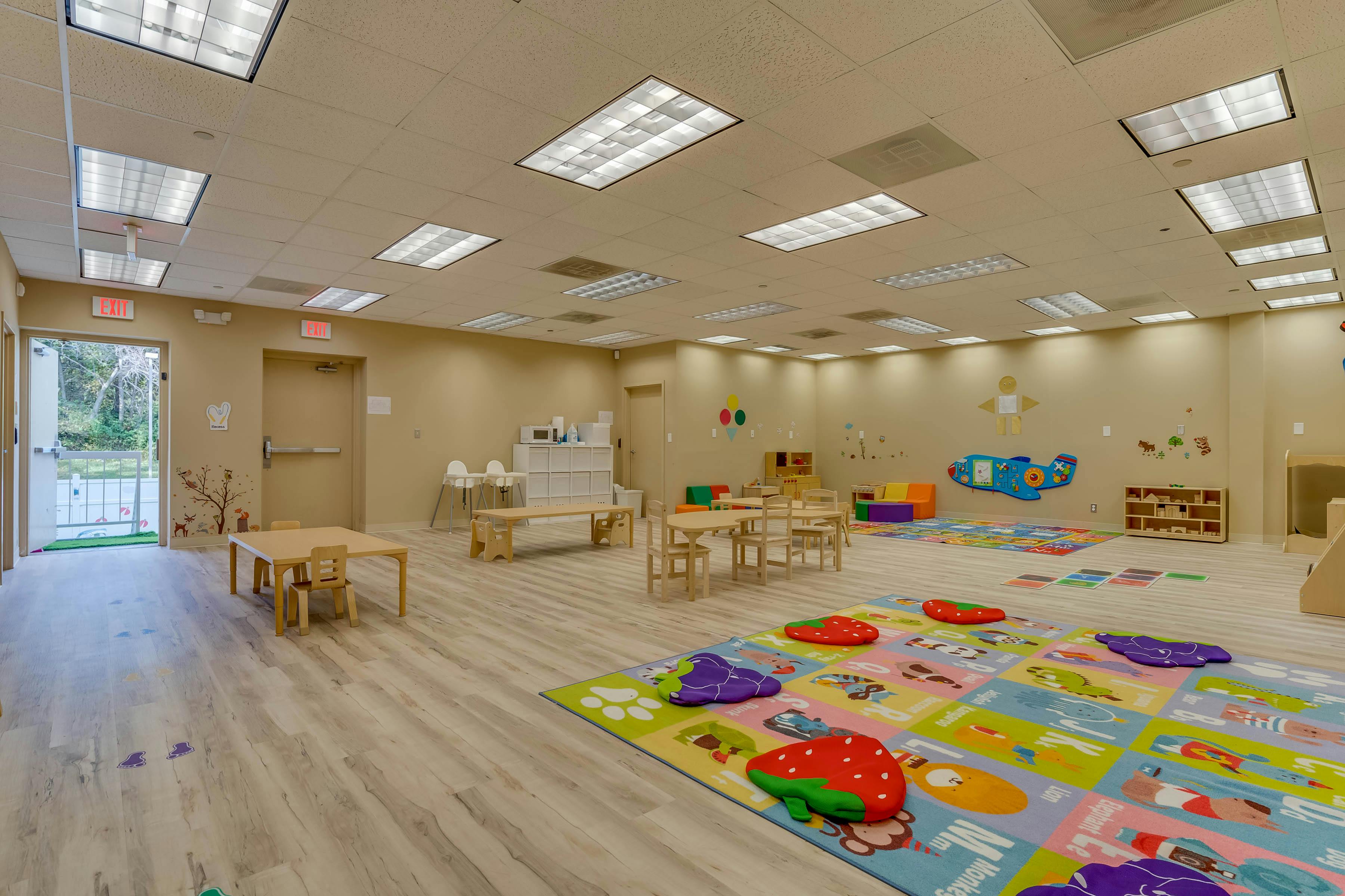 Empty classroom with small tables and chairs, colorful playmat on the floor