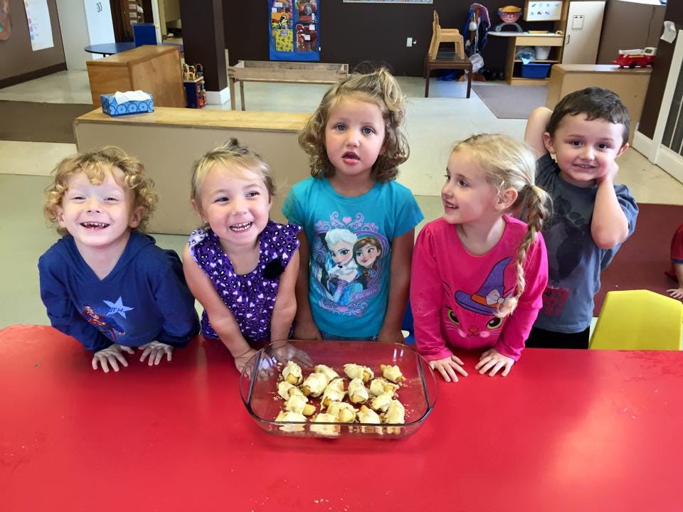 Five children standing behind a red table with a dish of food