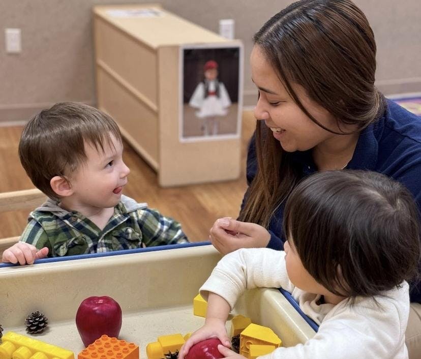 Adult and two children playing with toys in a classroom