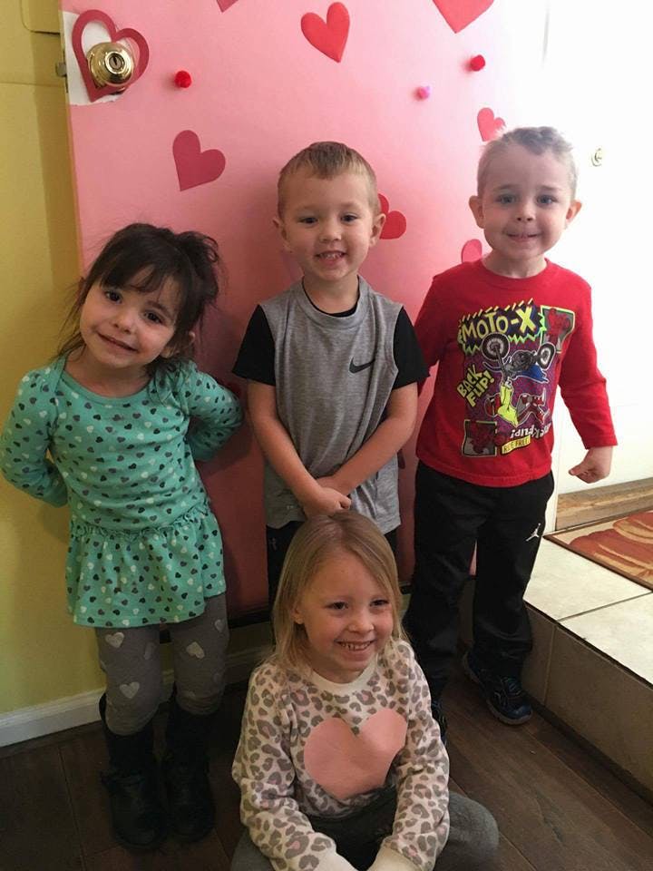 Four children posing in front of a pink door decorated with hearts