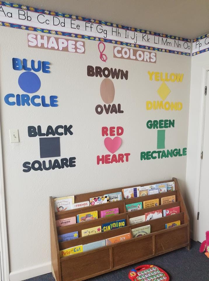 Classroom wall with shapes and colors chart above a wooden book display