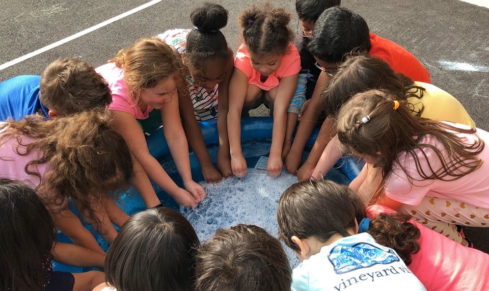 Children gathered around a small pool, hands in water