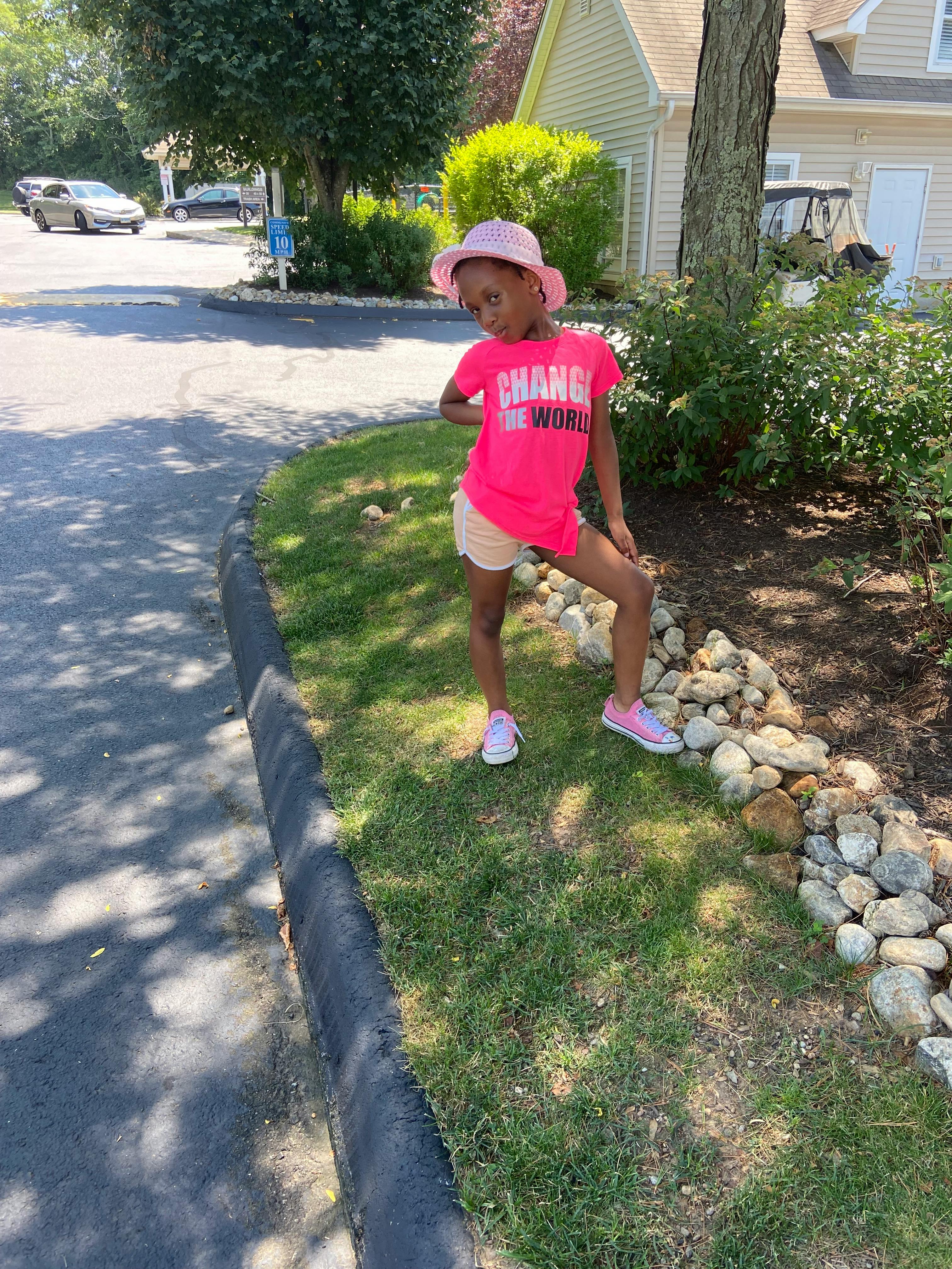 Child in a pink shirt and hat standing on grass