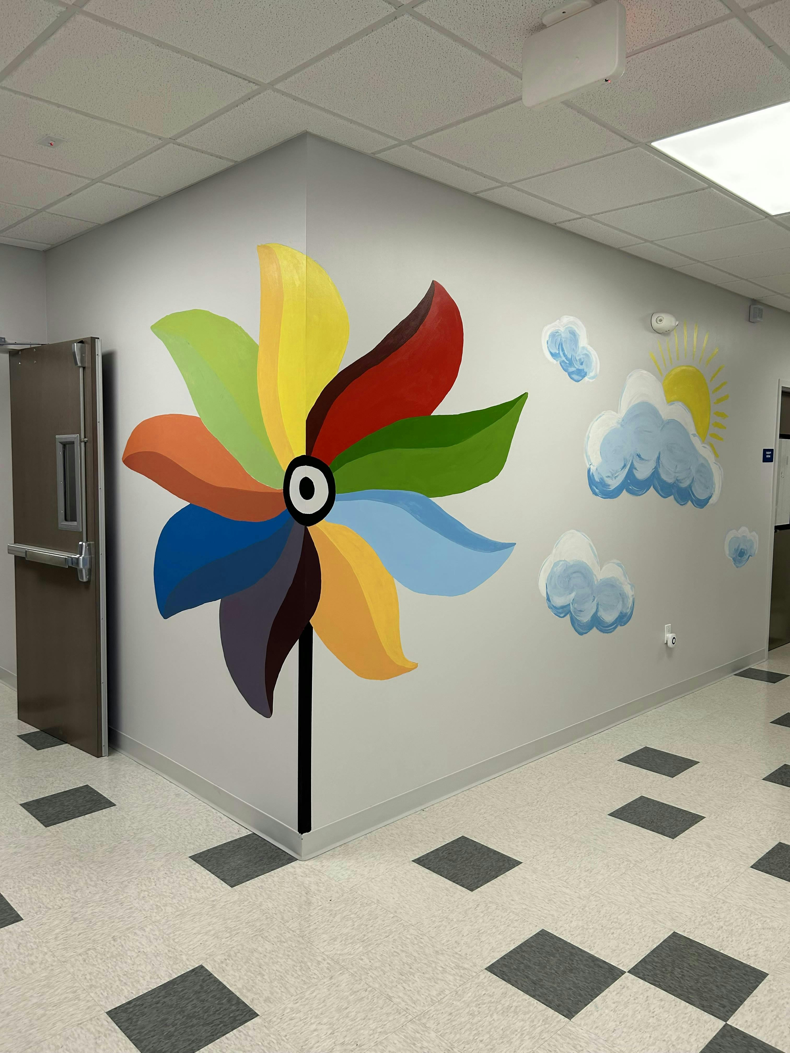 Colorful pinwheel mural on a wall with clouds and sun painted sun