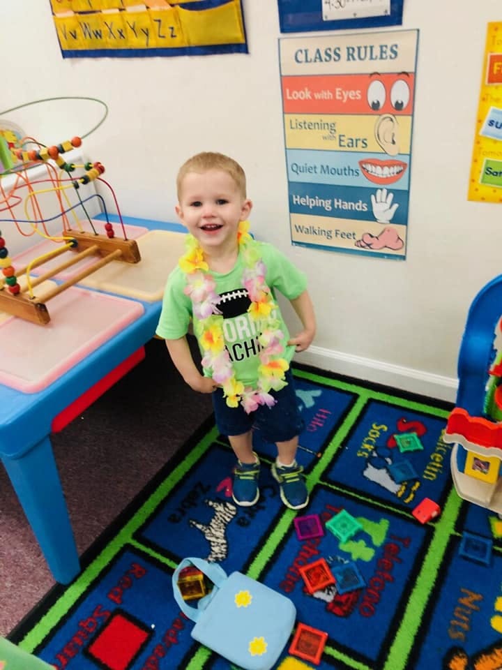 Child wearing a lei standing on a rug in a classroom