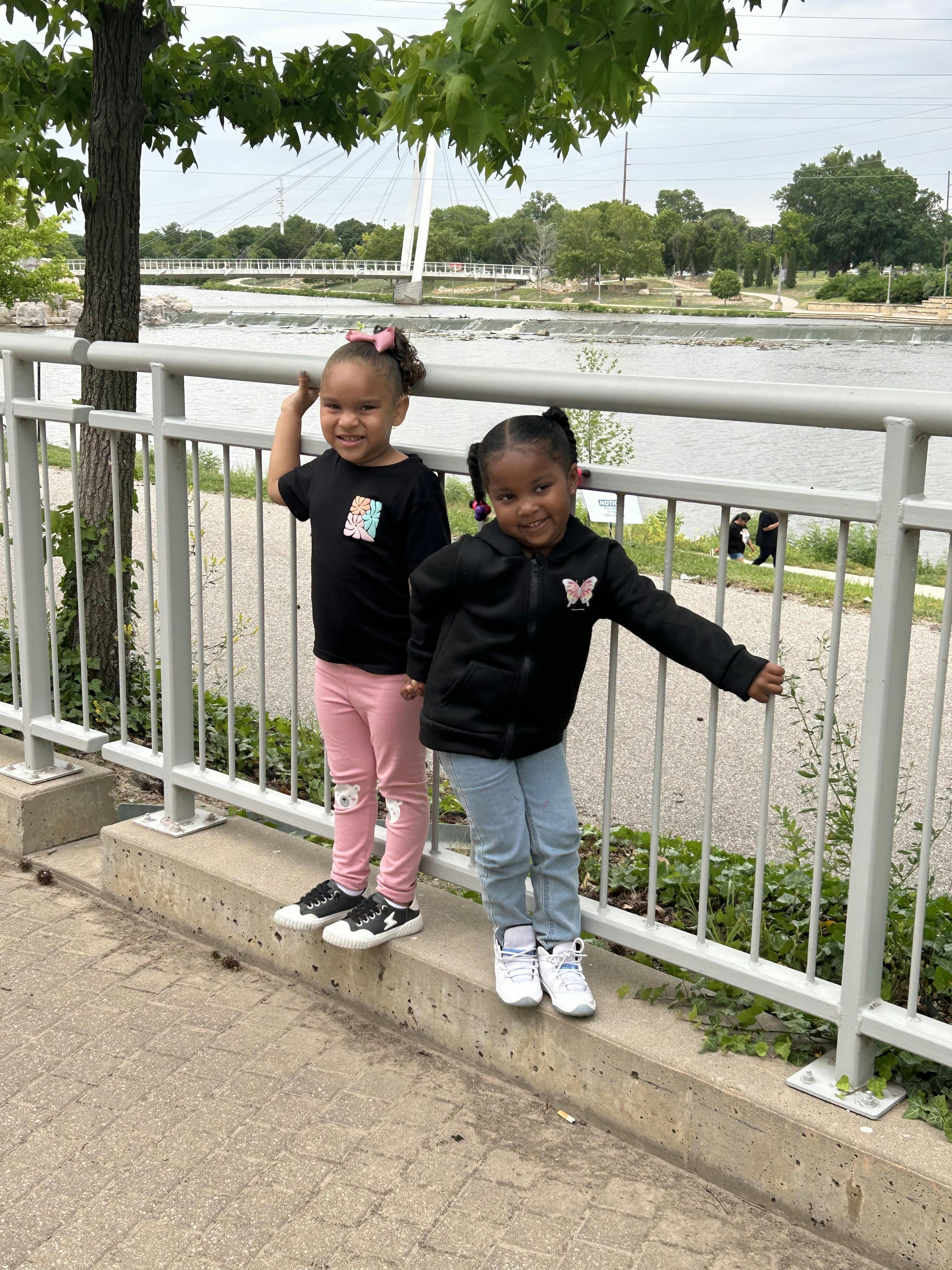 Two children standing on a ledge next to a fence overlooking a river