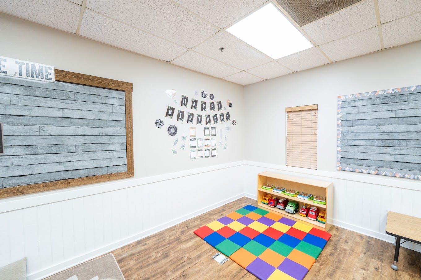 Classroom corner with birthday decorations and a toy shelf on a colorful mat