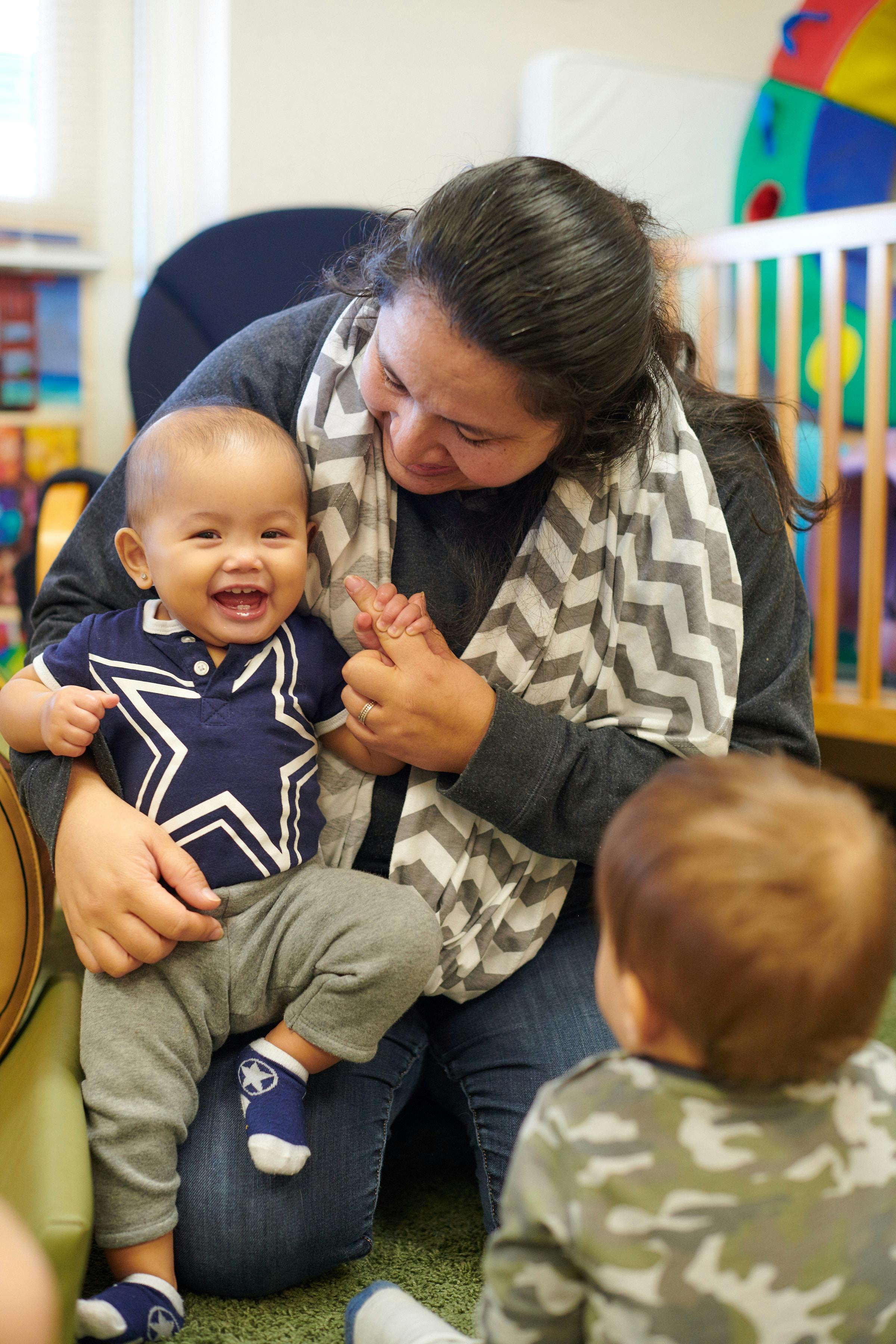 Person kneeling, holding a laughing child, with another child in foreground