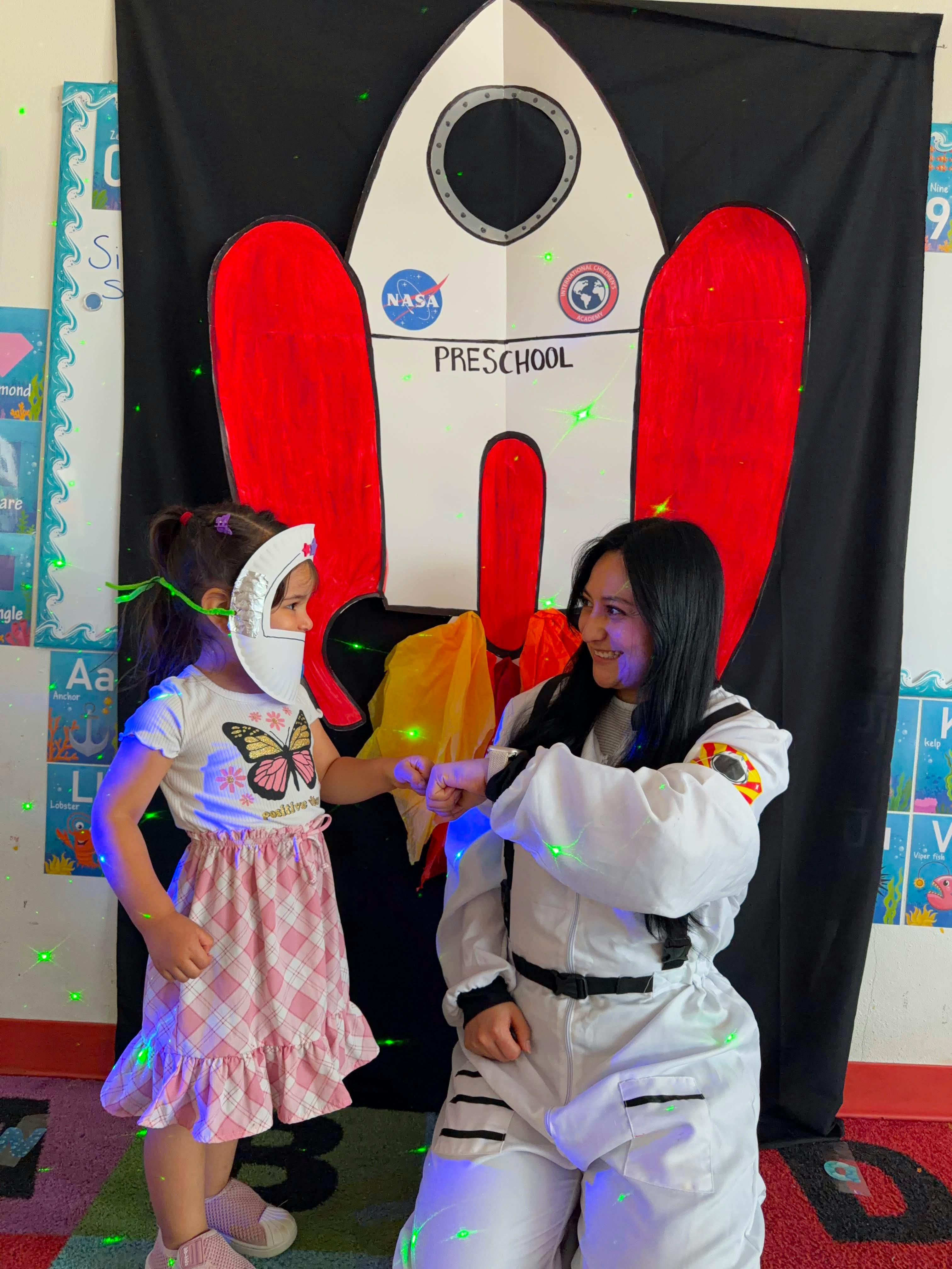 Child and person in astronaut costume fist bumping in front of rocket backdrop