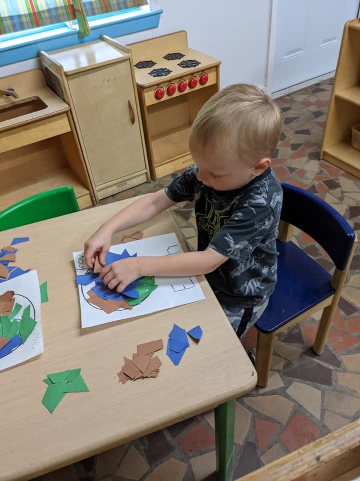 Child sitting at a table doing a paper craft in a classroom