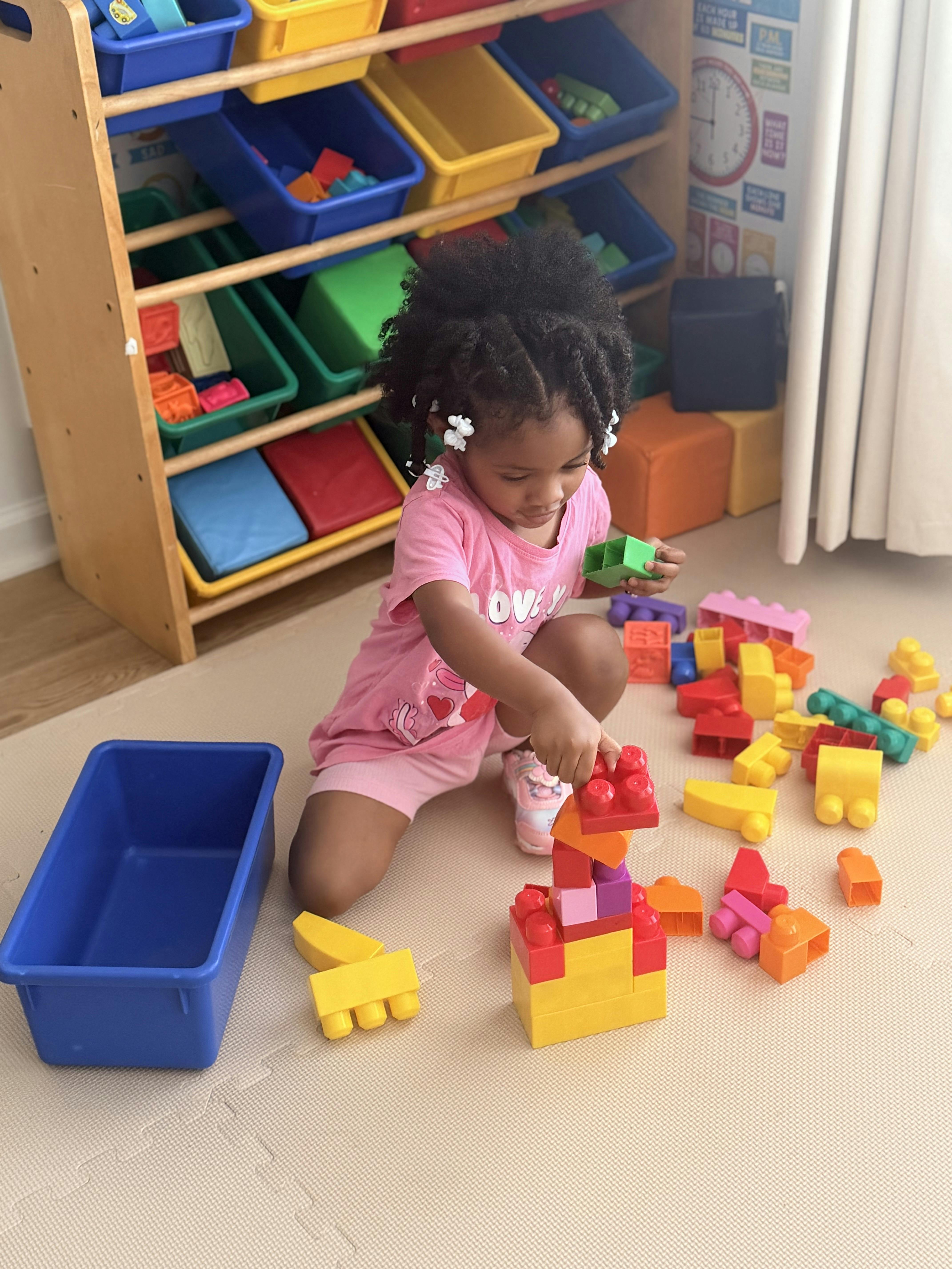 Child building a tower with colorful plastic blocks on a playroom floor