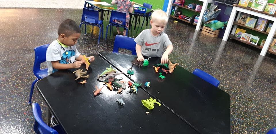 Two children playing with toy dinosaurs at a table