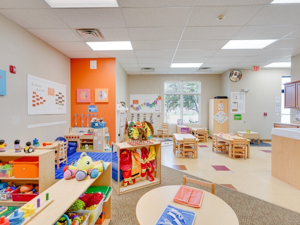 A colorful classroom with small tables and chairs, toys, and educational displays