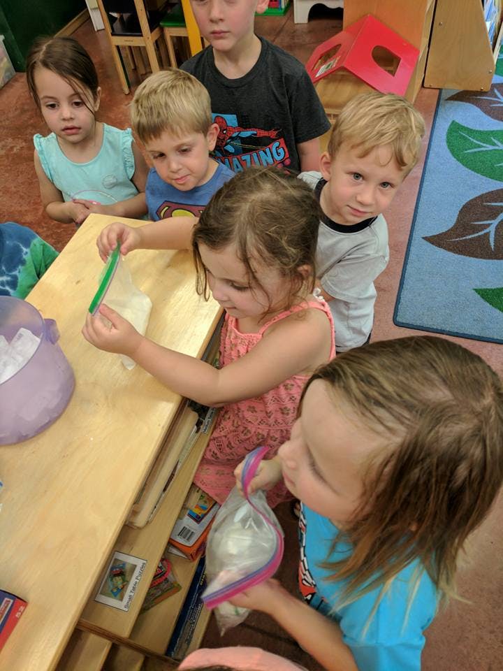 Children gathered around a table, one child holding a plastic bag