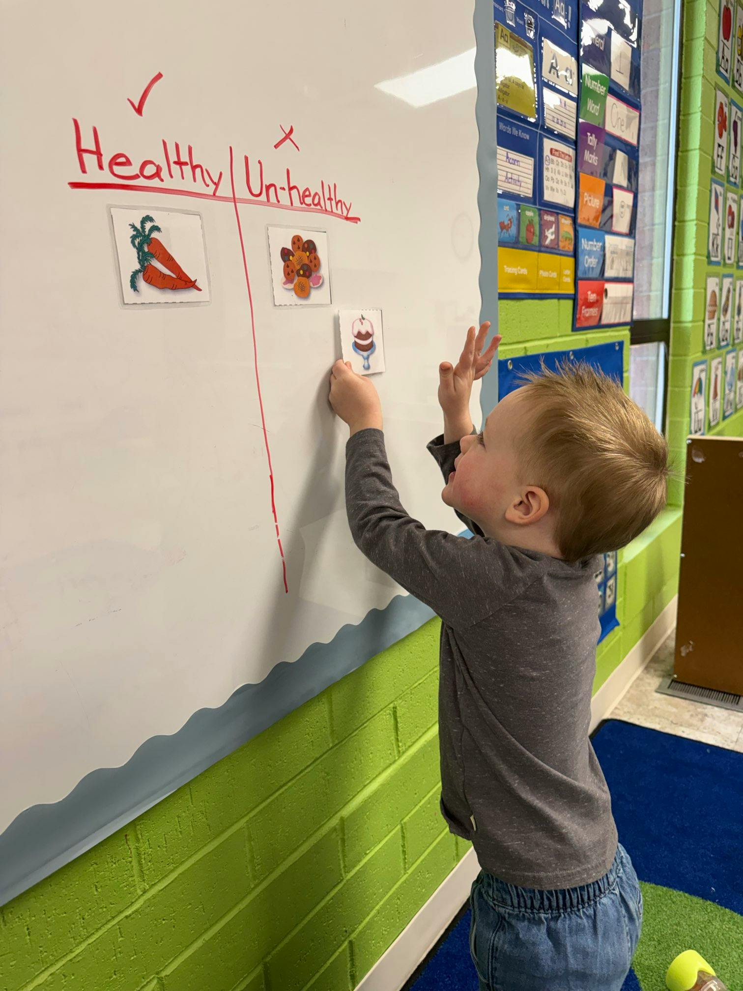 Child placing an "unhealthy" food picture under "Un-healthy" on a whiteboard