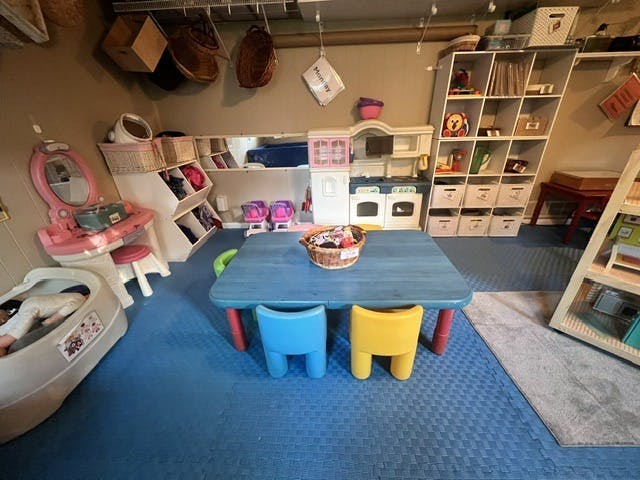 Playroom with a blue table, colorful chairs, and toy storage units