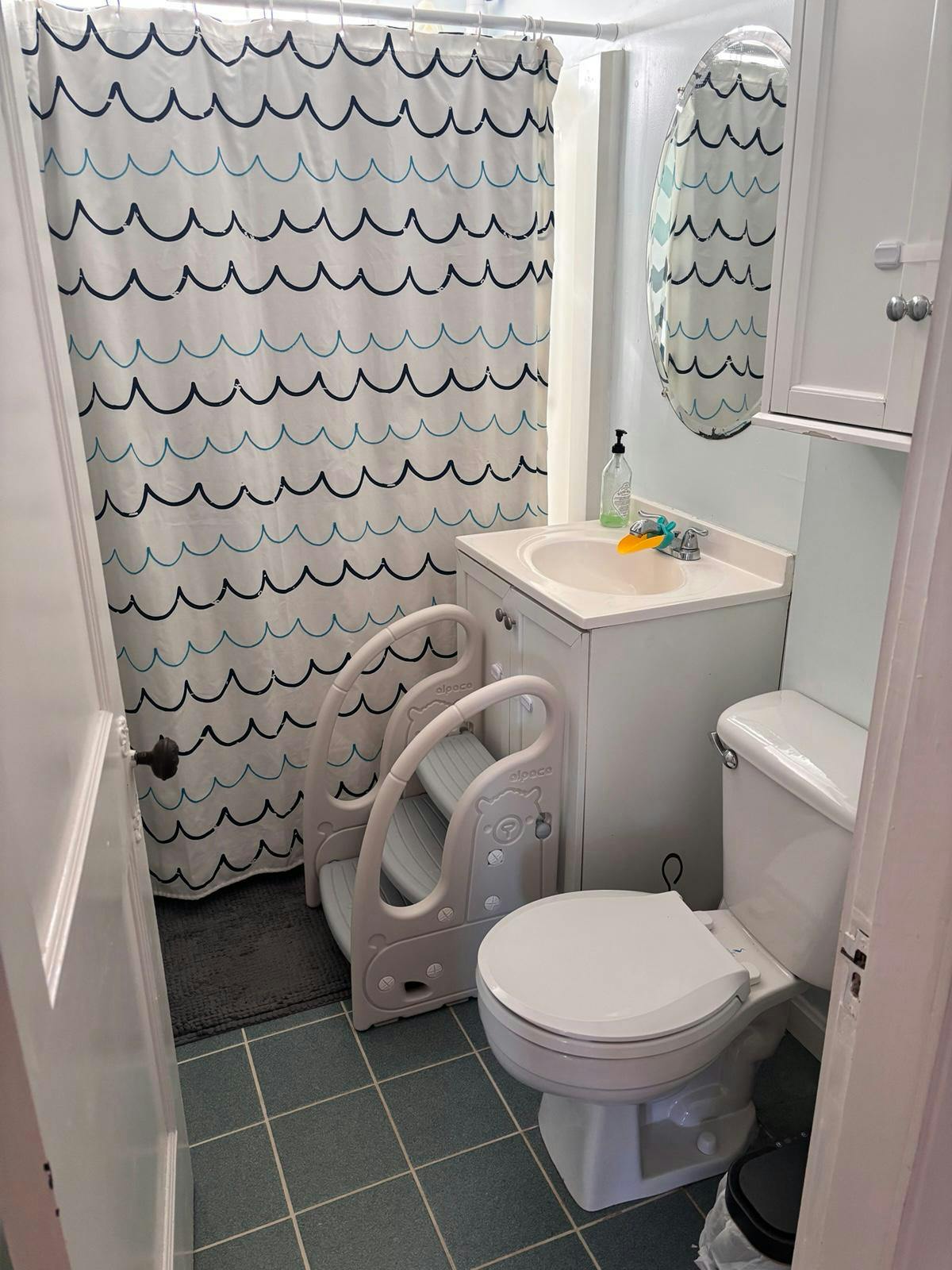 Bathroom with a wave patterned shower curtain and a toddler step stool