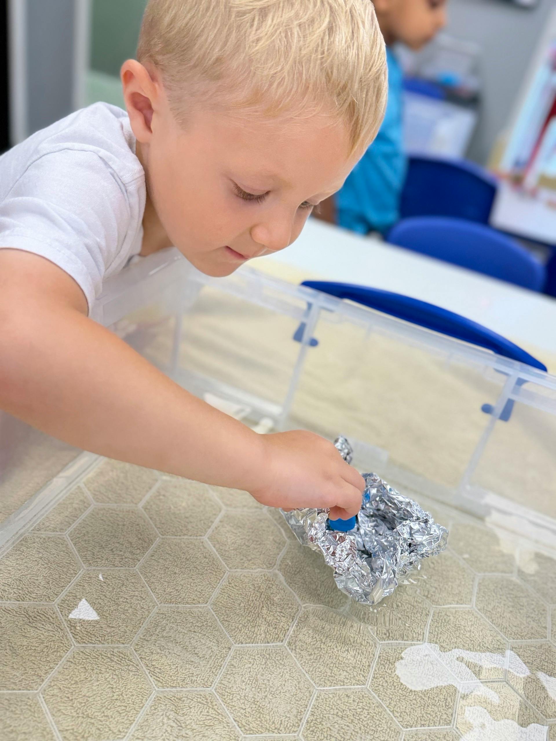 Child playing with a small foil boat in a water tray