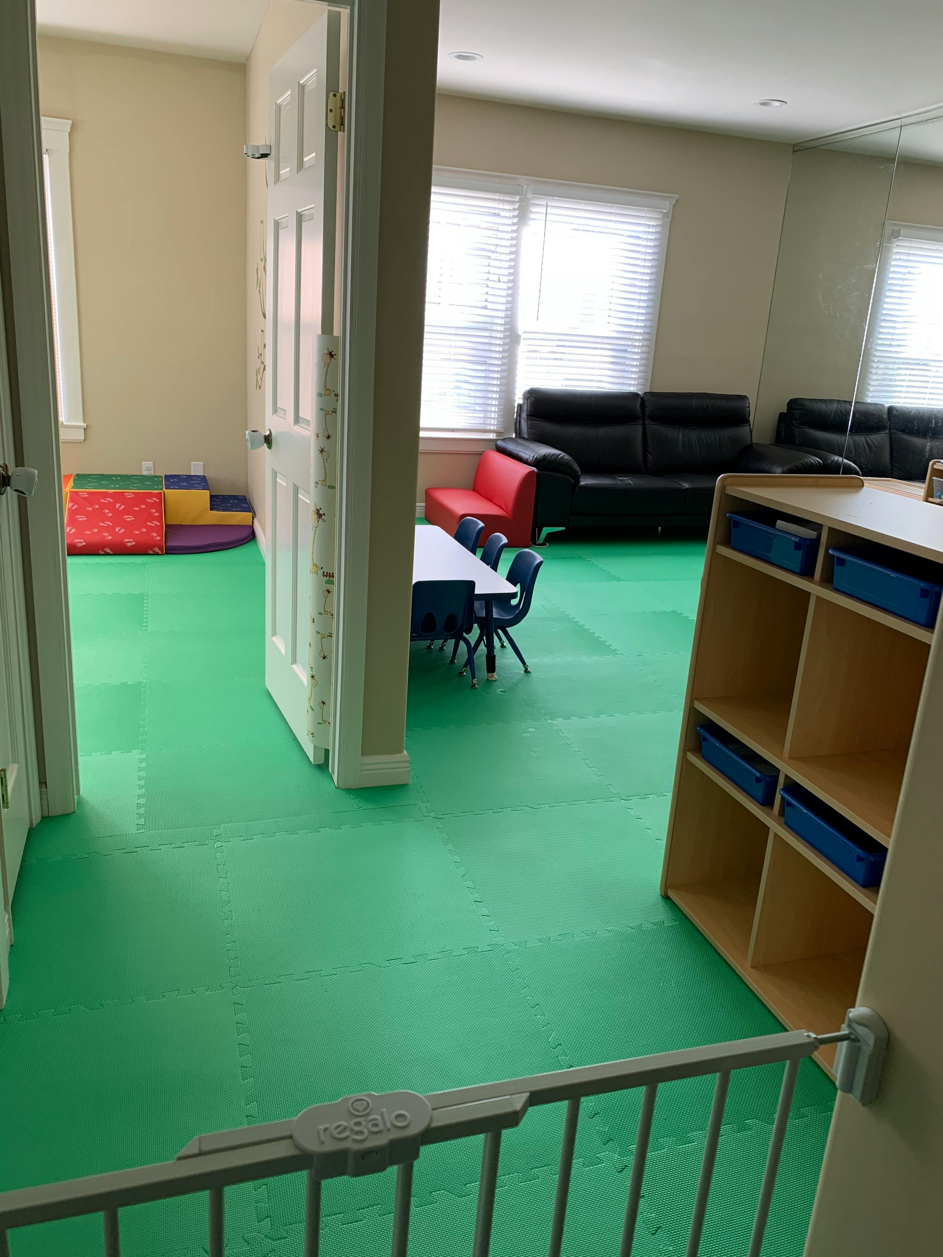 Room with green floor, child-sized table and chairs, and soft play mats