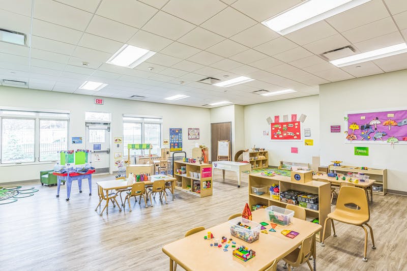 An empty, brightly lit classroom with small tables, chairs, and play equipment