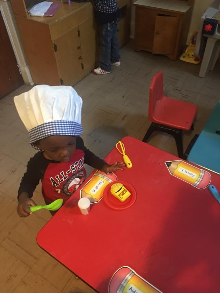 Child in a chef hat playing with toy food at a red table
