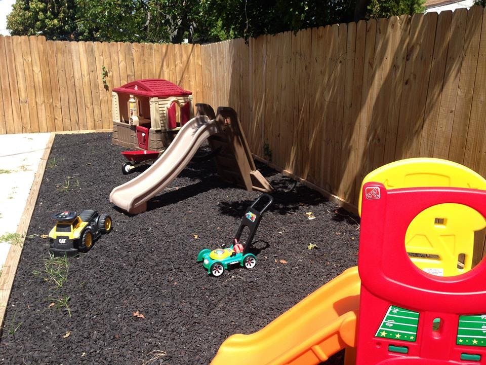 Playground with a slide, playhouse, and toy vehicles on dark ground cover