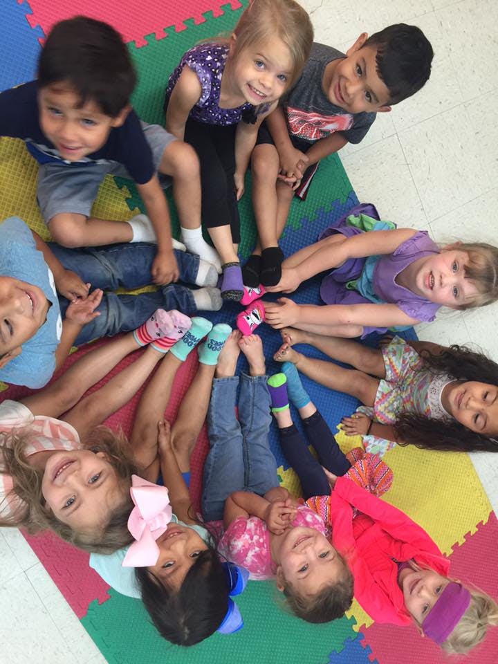 Group of children sitting in a circle with their feet touching in the center