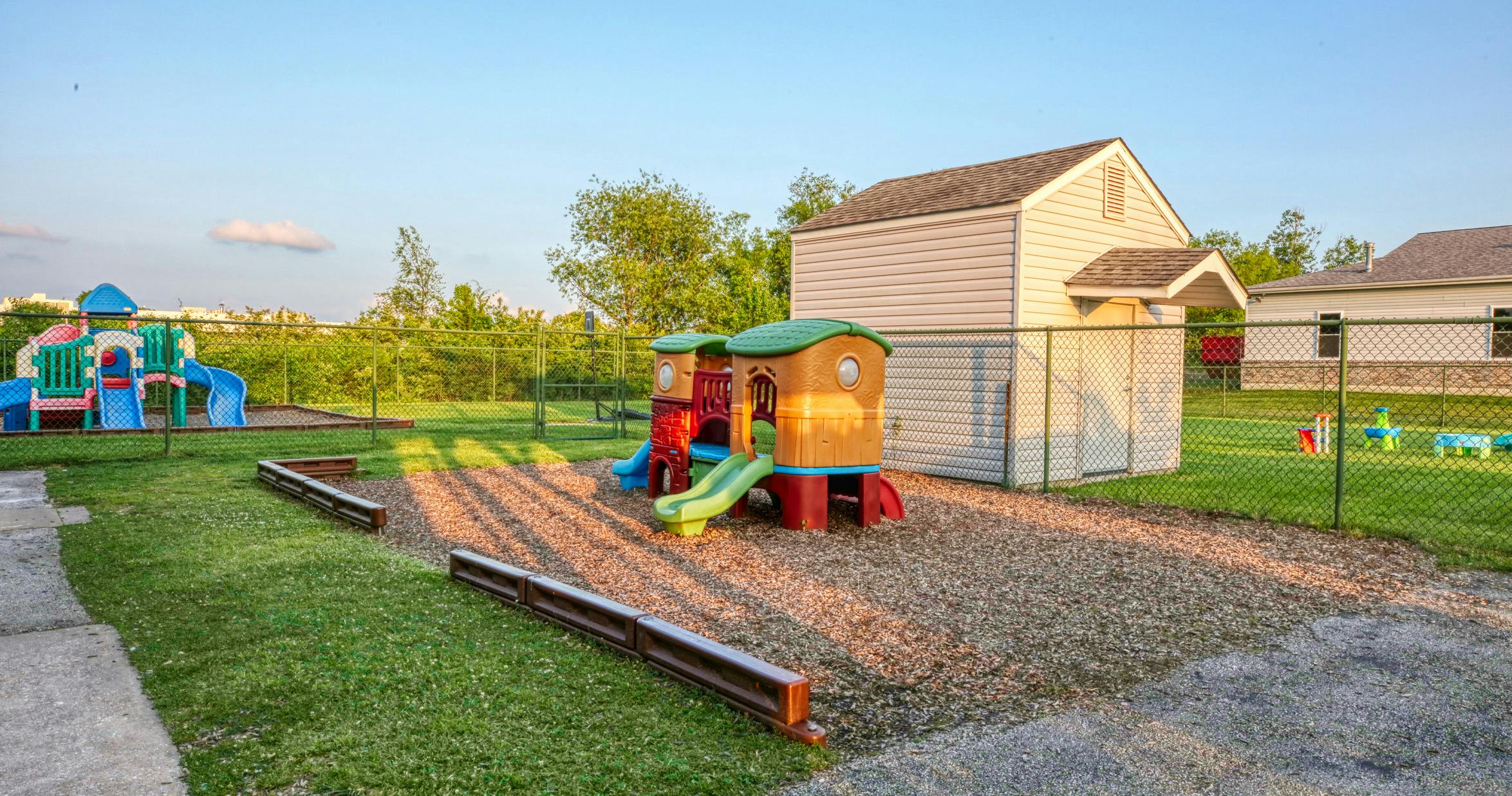 Playground with two play structures on wood chips, fenced-in yard