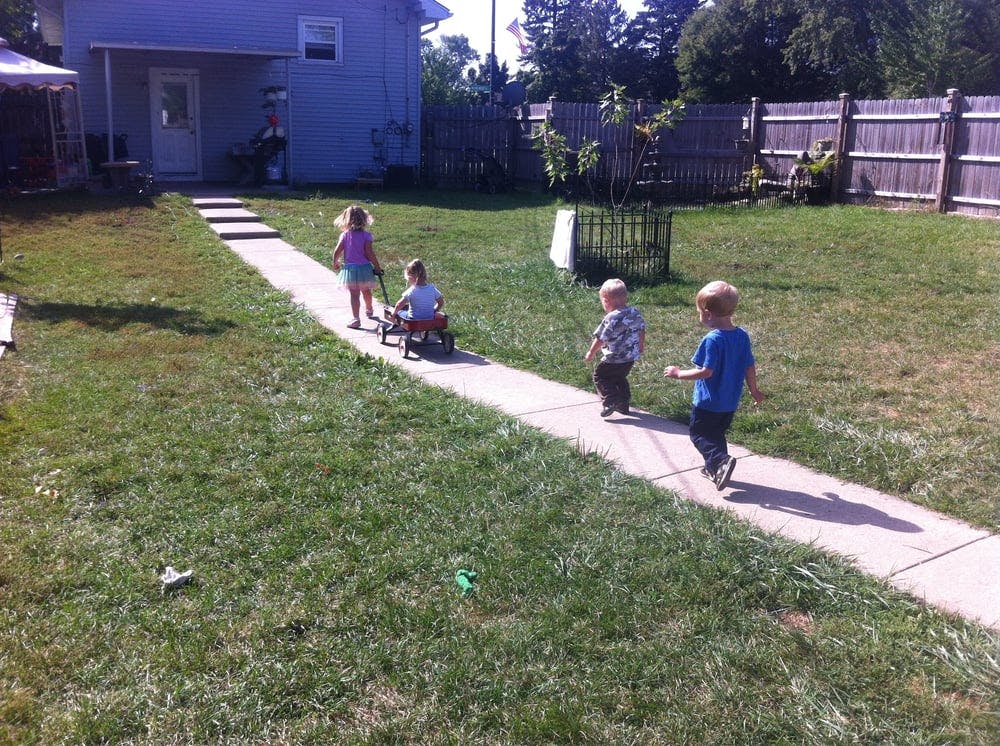 Children playing on a sidewalk in a grassy yard