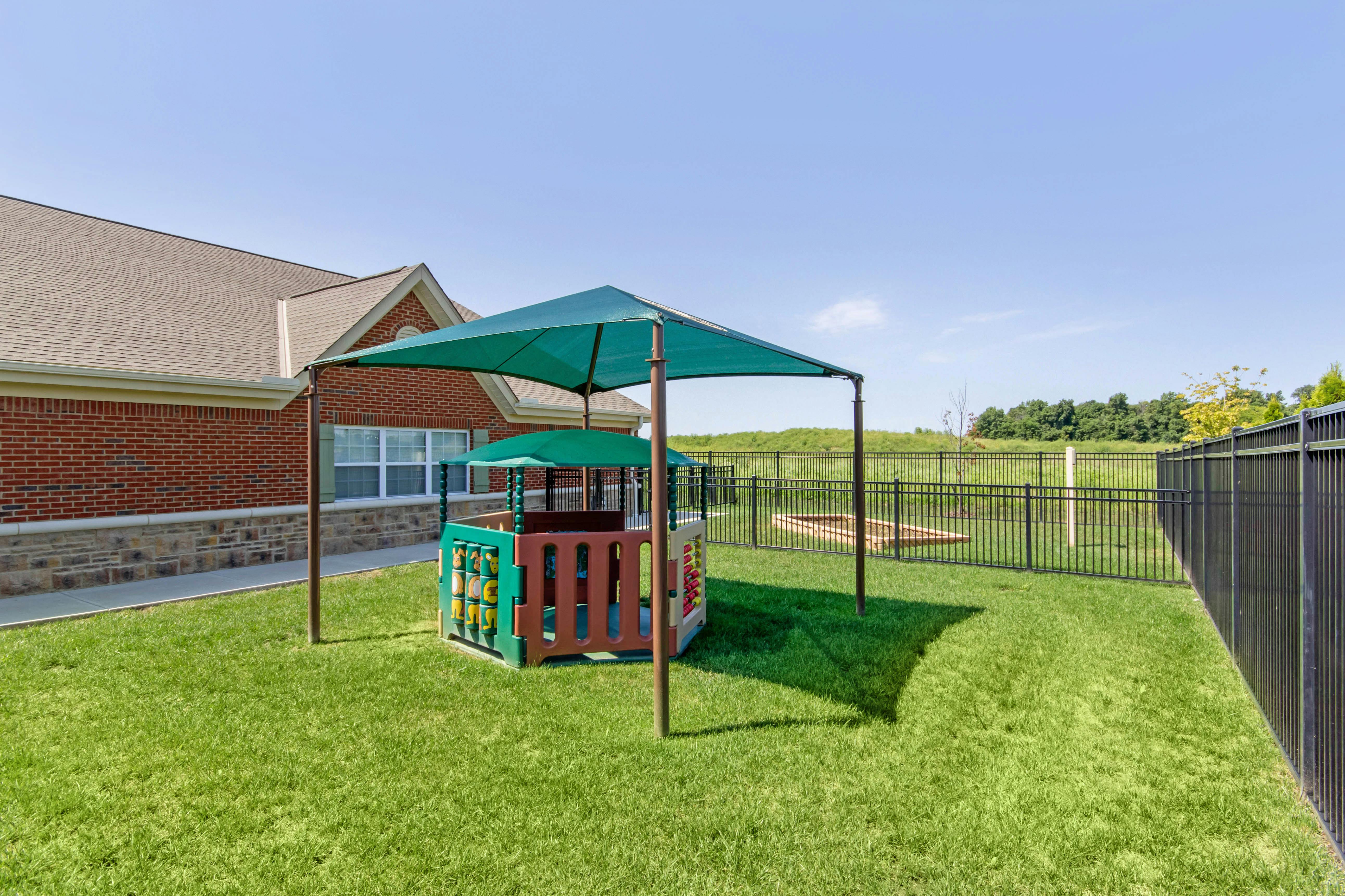 Childcare playground with a play structure under a large green shade canopy