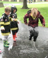 Three children playing in puddles, one jumping