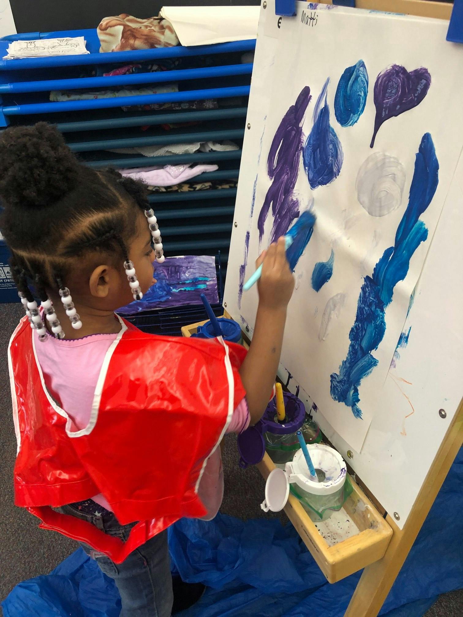 Child in a red smock painting on an easel