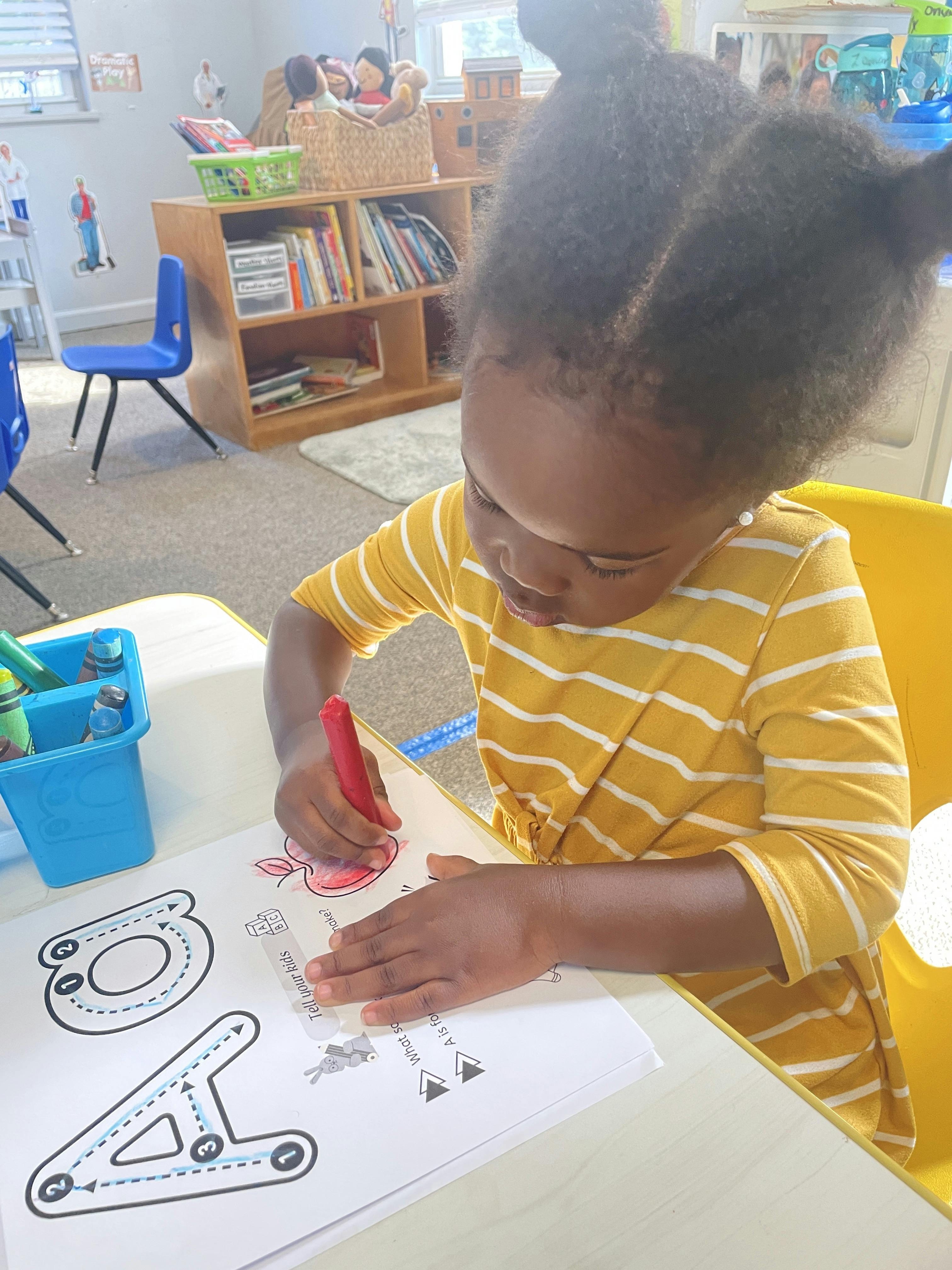 Child coloring an apple illustration on a worksheet in a classroom