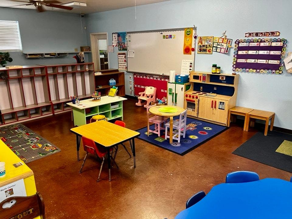 Classroom with small tables and chairs, play kitchen, and whiteboard