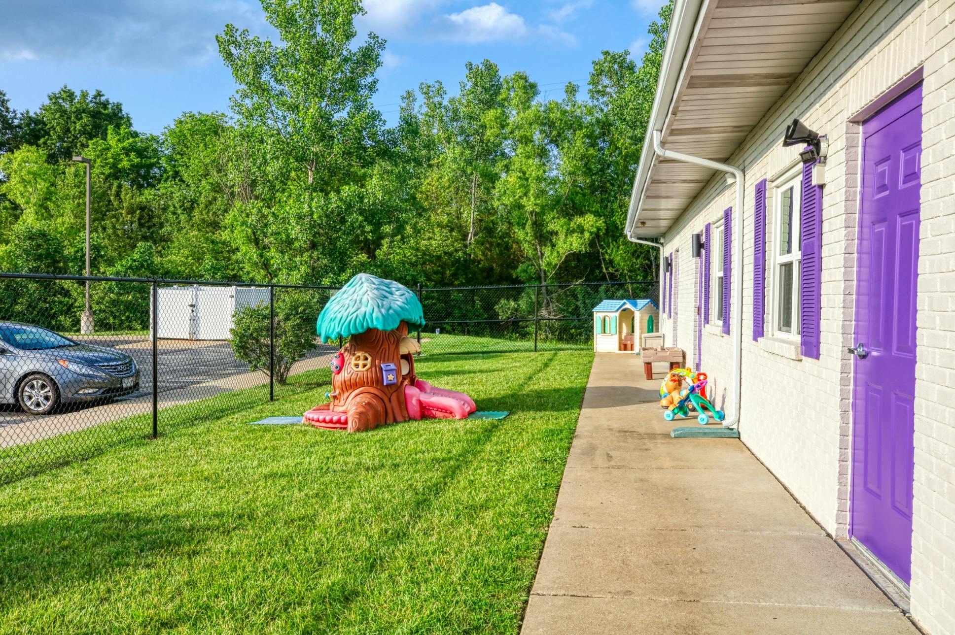 Outdoor play area with a white building, purple doors, and toy treehouse and slide