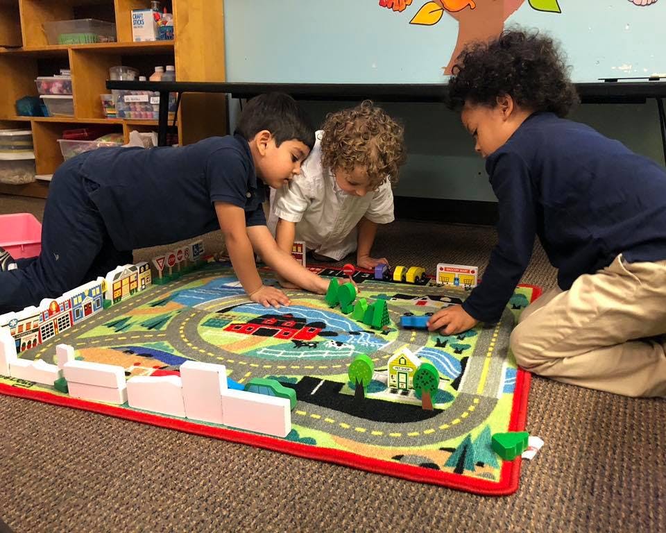 Three children playing with toy cars on a road map rug