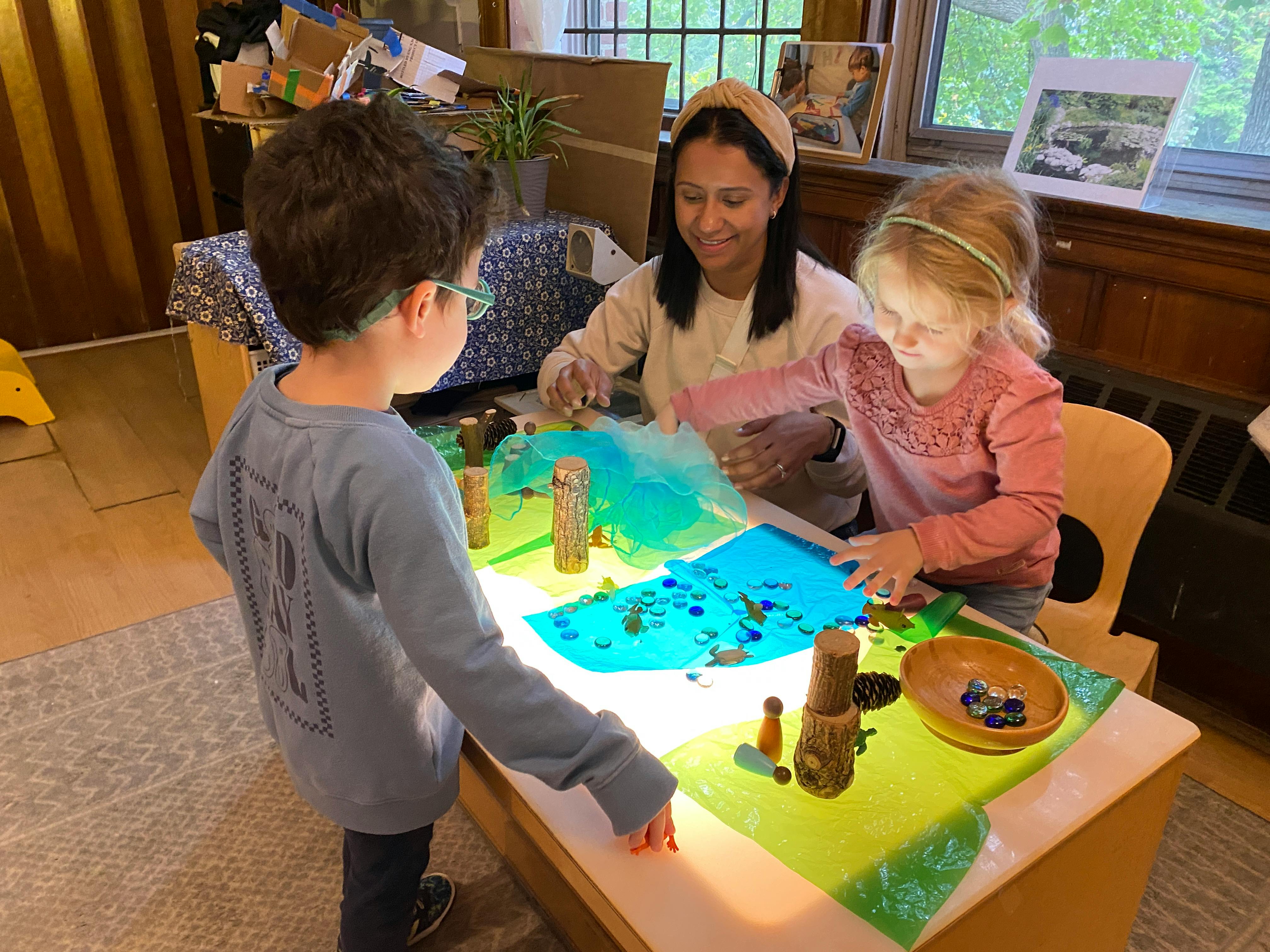 Adult and two children playing with translucent materials on a light table
